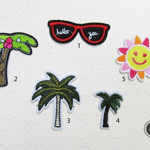 Könnte beinhalten: Fünf gestickte Bügelbilder mit Sommermotiv. Die Patches beinhalten eine Palme, eine Sonnenbrille mit den Worten "hello" und "you", eine weitere Palme, eine kleinere Palme und eine gelbe Sonne mit einem Smiley.