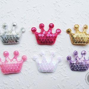 Könnte beinhalten: Sechs glitzernde Kronen-förmige Verzierungen in verschiedenen Farben, darunter Silber, Pink, Gold und Lila. Die Kronen bestehen aus Pailletten und sind perfekt, um Bastelarbeiten und Projekten einen Hauch von Glanz zu verleihen.