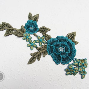 Könnte beinhalten: Türkise und goldene gestickte Blumenapplikation mit einer großen Blume und kleineren Blumen und Blättern.