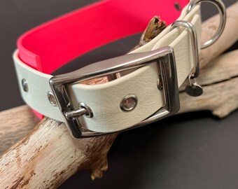 May include: A two-toned collar featuring a bright neon pink interior and a textured off-white exterior. The collar includes a silver-toned metal buckle, metal eyelets for adjustment, and a D-ring attachment point for a leash or identification tag.
