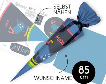 May include: A blue and red monster-themed school cone with the name "MAXI" printed on it. The cone is 85 cm long and is made of fabric. The cone is ready to be sewn together. The image also includes a pattern for the cone.