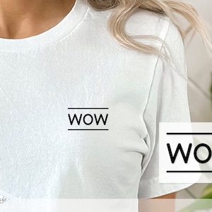 Könnte beinhalten: Weißes T-Shirt mit dem Wort "WOW" in Schwarz auf der Vorderseite. Das Wort ist von zwei horizontalen Linien eingerahmt.