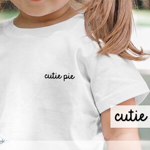 Könnte beinhalten: Weißes T-Shirt mit dem Aufdruck "cutie pie" auf der Vorderseite.