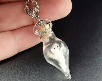 May include: A silver chain necklace with a glass bottle pendant. The bottle is clear and contains a small white ghost figurine.