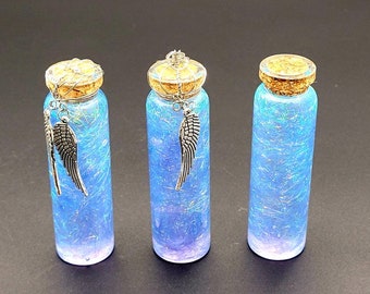 May include: Three small glass bottles with cork tops and silver angel wing charms. The bottles are filled with iridescent blue glitter.