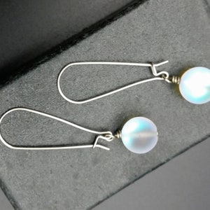 May include: A pair of silver dangle earrings with iridescent white glass beads.