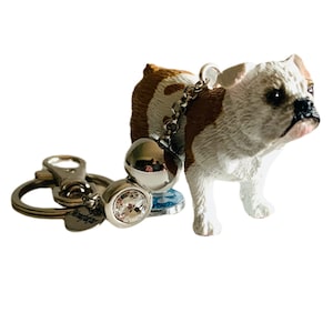 May include: A white and brown bulldog figurine keychain with a silver chain and a clear crystal charm. The keychain also has a silver ring and a silver clasp.