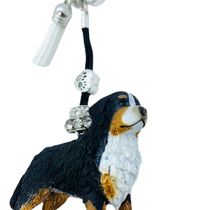 Könnte beinhalten: Ein schwarzer, weißer und brauner Berner Sennenhund-Figuren-Schlüsselanhänger mit einem silbernen Anhänger und einem weißen Quasten. Der Schlüsselanhänger hat einen blauen Kristall-Anhänger und einen silbernen Pfotenabdruck-Anhänger.