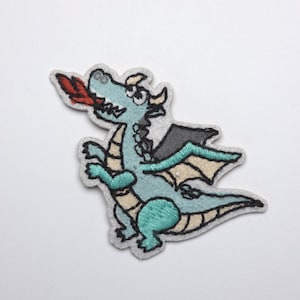 Könnte beinhalten: Ein gestickter Aufnäher mit einem Cartoon-Drachen. Der Drache ist hellblau mit türkisfarbenen Akzenten, grauen Flügeln und einer roten Flamme. Der Aufnäher hat einen grauen Rand und ist für Kleidung oder Accessoires geeignet.
