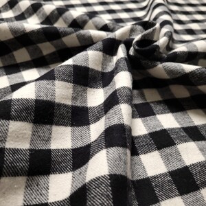 May include: Black and white checkered fabric with a soft, textured feel. The fabric is folded and draped, showcasing its pattern and texture.
