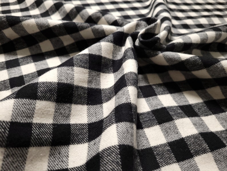 May include: Black and white checkered fabric with a soft, textured feel. The fabric is folded and draped, showcasing its pattern and texture.
