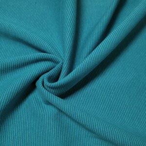 Puede incluir: Primer plano de una tela color teal con textura acanalada. La tela est&aacute; doblada, mostrando las acanaladuras verticales. El color es un teal vibrante y s&oacute;lido, con sutiles variaciones tonales debido a los pliegues.