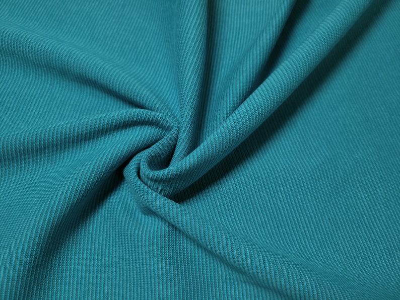 Puede incluir: Primer plano de una tela color teal con textura acanalada. La tela est&aacute; doblada, mostrando las acanaladuras verticales. El color es un teal vibrante y s&oacute;lido, con sutiles variaciones tonales debido a los pliegues.