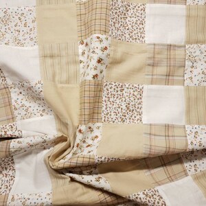 Könnte beinhalten: Eine Patchwork-Decke mit beigefarbenem Hintergrund und verschiedenen Blumenmustern in Braun-, Weiß- und Cremetönen.
