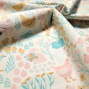 Könnte beinhalten: Ein weißer Stoff mit einem sich wiederholenden Muster aus pastellrosa und blauen Küken, Hasen und Eiern. Der Hintergrund ist hellcremefarben mit kleinen floralen Akzenten.