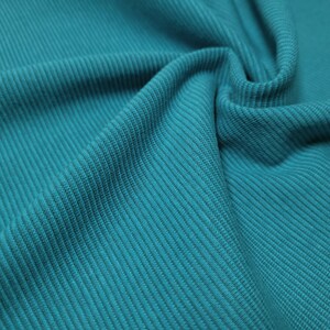 Puede incluir: Primer plano de una tela turquesa con textura acanalada. La tela est&aacute; doblada, mostrando la direcci&oacute;n diagonal de las acanaladuras. El color es un turquesa vibrante y s&oacute;lido, adecuado para ropa o decoraci&oacute;n del hogar.