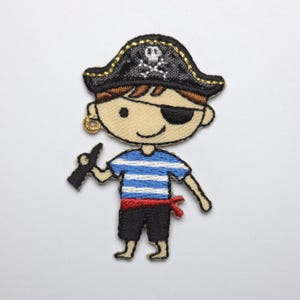 Könnte beinhalten: Gestickter Aufnäher eines Cartoon-Piraten. Der Pirat trägt einen schwarzen Hut mit Totenkopf, eine Augenklappe und ein blau-weiß gestreiftes Hemd. Er hält einen schwarzen Gegenstand und hat einen roten Schärpe.