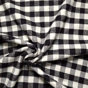 May include: Black and white checkered fabric with a textured surface. The fabric is folded and draped, creating a soft, flowing look.