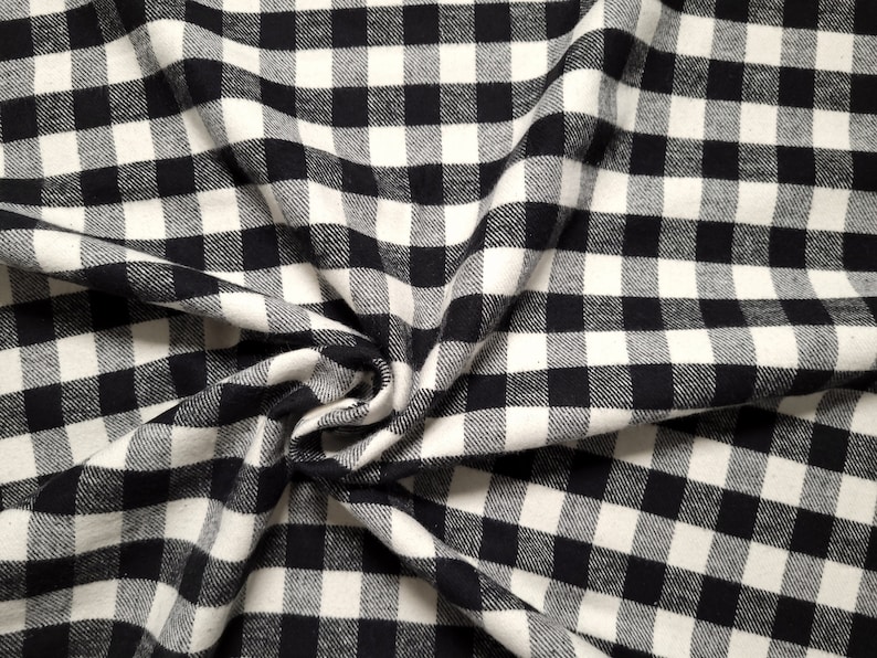 May include: Black and white checkered fabric with a textured surface. The fabric is folded and draped, creating a soft, flowing look.