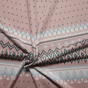 Könnte beinhalten: Nahaufnahme eines Stoffes mit sich wiederholendem geometrischen Muster in den Farbtönen Staubrosa, Weiß, Grau und Türkis. Der Stoff hat ein strukturiertes Aussehen und ist gefaltet, wodurch das komplizierte Design sichtbar wird. Das Muster umfasst Zickzacklinien, Rauten und gepunktete Linien.
