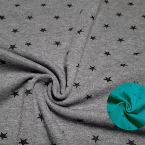 Könnte beinhalten: Grauer Stoff mit einem schwarzen Sternenmuster. Eine Nahaufnahme des Stoffes zeigt eine blaugrüne Farbe.