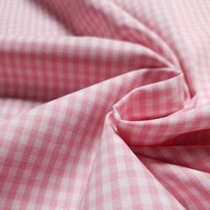 Könnte beinhalten: Rosa-weißes Gingham-Gewebe mit feinem Karomuster. Der Stoff ist gefaltet und drapiert und zeigt die Textur und die Webart.
