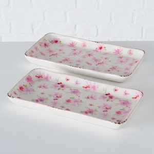 Könnte beinhalten: Zwei rechteckige Serviertabletts aus Keramik mit weißem Hintergrund und einem rosafarbenen Blumenmuster.