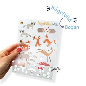 Könnte beinhalten: Ein transparenter Bogen mit Bügelbildern, der verschiedene Waldtiere wie Waschbären, Igel, Füchse, ein Reh, Wildschweine, Bienen und Pilze zeigt. Auf dem Bogen ist der Text Bügelbilder sowie JaTiJu aufgedruckt.