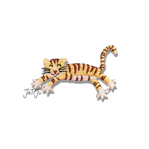 Könnte beinhalten: Gestickter Aufnäher eines Zeichentricktigers in Laufpose. Der Tiger hat gelbe und braune Streifen, ein lächelndes Gesicht und ausgestreckte Pfoten. Der Aufnäher befindet sich auf weißem Hintergrund. Der Text "JatiJu" befindet sich in der unteren linken Ecke.