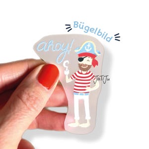Könnte beinhalten: Ein transparenter Aufkleber mit einem Cartoon-Piraten-Design. Der Pirat trägt ein rot-weiß gestreiftes Oberteil, eine Augenklappe und einen blauen Piratenhut. Die Wörter "ahoy!" und "Bügelbild" sind aufgedruckt.