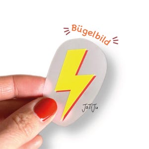 Könnte beinhalten: Ein gelber Blitz mit roter Umrandung auf einem transparenten, ovalen Bügelbild. Der Text "Bügelbild" befindet sich oberhalb des Designs, und der Name "JatiJu" steht darunter.