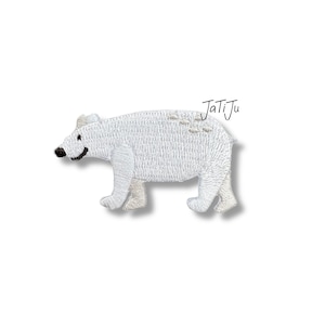 Könnte beinhalten: Gestickter weißer Eisbär-Aufnäher mit schwarzen Augen und einem lächelnden Mund. Der Bär hat ein strukturiertes Aussehen und geht auf allen Vieren. Der Text "JatiJu" ist in schwarzer Schreibschrift oben rechts geschrieben.