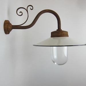 May include: A white enamel outdoor wall light fixture with a clear glass globe and a rusty metal arm with a decorative scroll design.