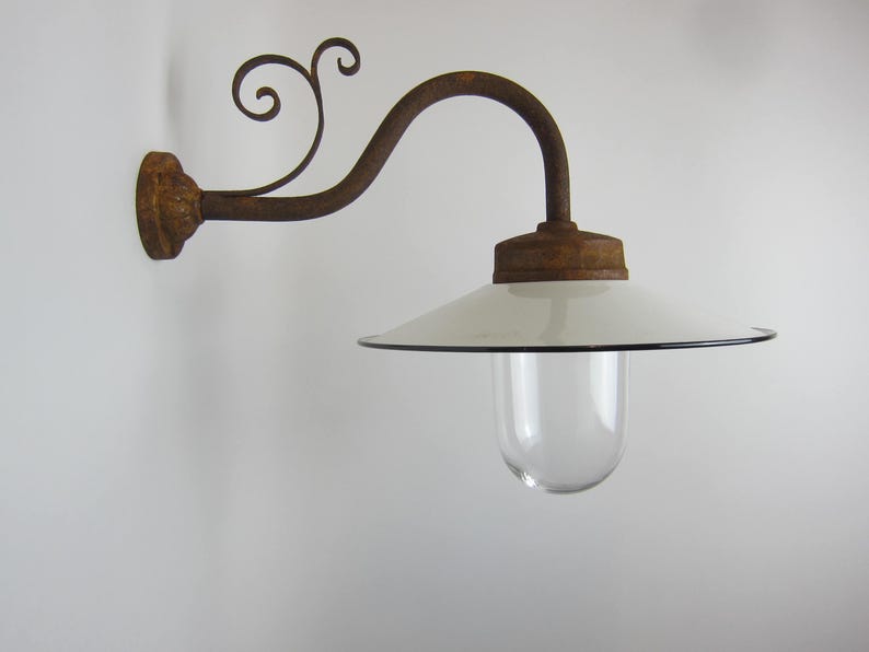 May include: A white enamel outdoor wall light fixture with a clear glass globe and a rusty metal arm with a decorative scroll design.