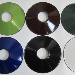 May include: Six round metal lampshades in different colors: green, brown, dark green, blue, black, and white. Each lampshade has a hole in the center.
