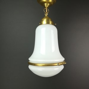 Op de afbeelding: Een witte glazen hanglamp met een messing afwerking. De lamp heeft een klokvormige kap met een decoratieve band in het midden.