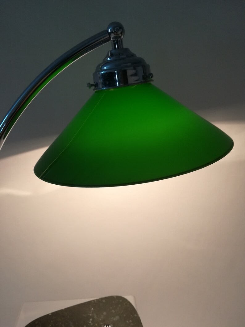 May include: A chrome desk lamp with a green glass shade. The lamp has a curved arm and a round base.
