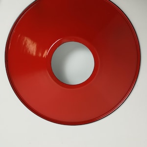 May include: A red metal lampshade with a black rim and a circular opening in the center.