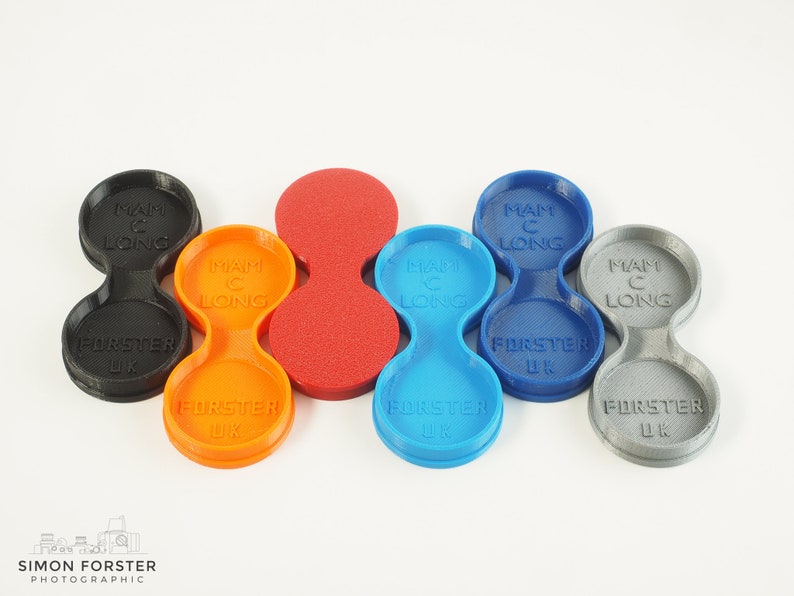 May include: Five 3D printed double-sided lens caps in different colours: black, orange, red, blue, and grey. Each cap has the text "MAM C LONG" and "FORSTER UK" printed on it.
