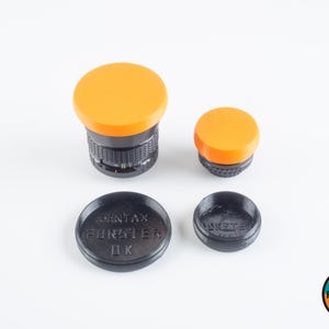 May include: Four camera lens caps, two orange and two black. The black caps have the text "PENTAX FORESTER ДК" printed on them.