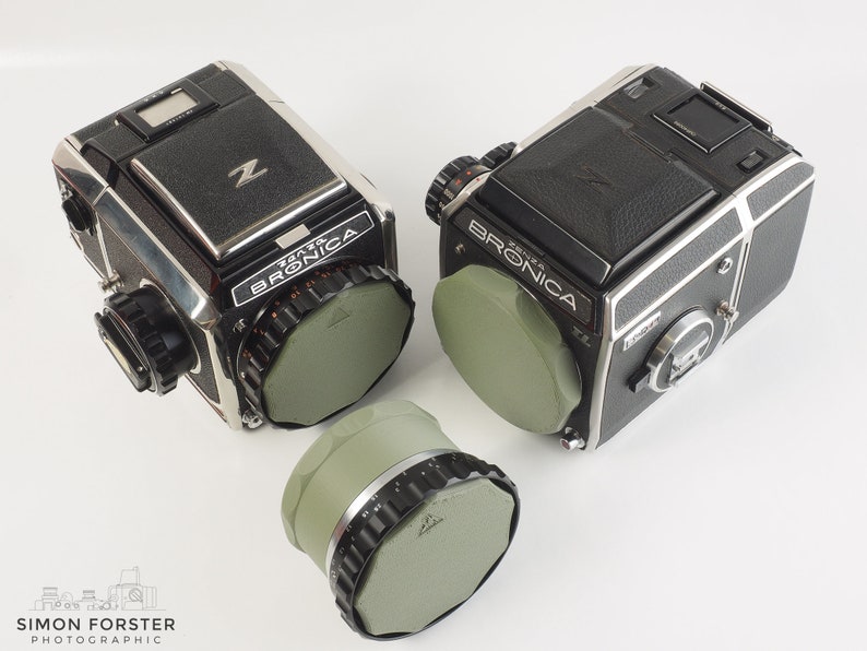May include: Two black and silver Bronica Zenza Bronica cameras with green lens caps. A third green lens cap is in the foreground.