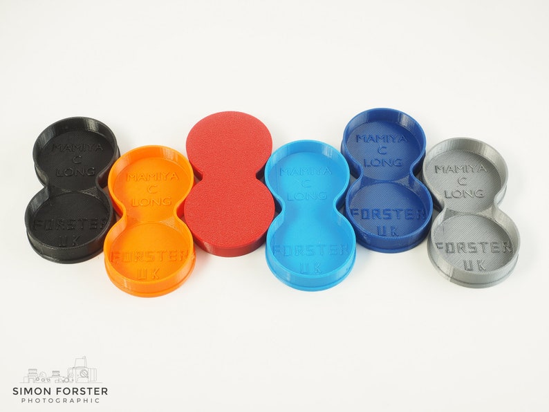 May include: Five 3D printed camera lens holders in different colours: black, orange, red, blue, and grey. Each holder has two compartments and is labelled "Mamiya C Long" and "Forster UK".