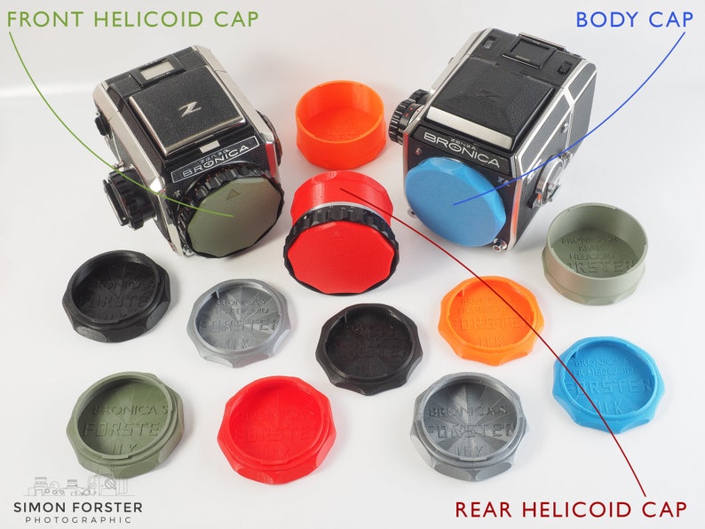 May include: A set of 10 camera lens caps in various colors, including black, gray, green, red, orange, and blue. The caps are labeled "Bronica's Forster" and are arranged in a circle around two cameras. The cameras are a black Bronica ETRS and a black Bronica Zenza Bronica.