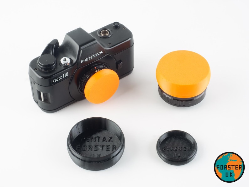May include: A black Pentax auto 110 camera with a bright orange lens cap. Three additional lens caps are shown: one orange and two black. The black lens caps have the text "Pentax" and "Forster UK" printed on them.