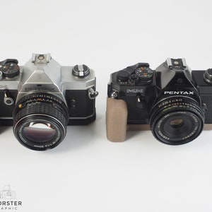 May include: Two silver and black Pentax film cameras with SMC Takumar lenses. The cameras are side by side on a white surface.