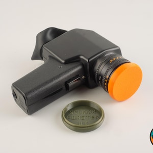 May include: A black and orange camera with a lens cap that says "SÖLIGER FORSTER UK".