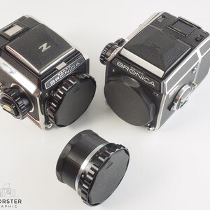 May include: Two black and silver Bronica ETRS cameras with a black lens cap on each. A black lens adapter is also pictured.