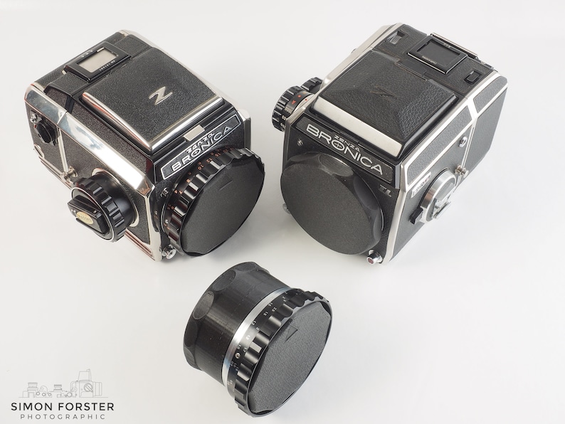 May include: Two black and silver Bronica ETRS cameras with a black lens cap on each. A black lens adapter is also pictured.