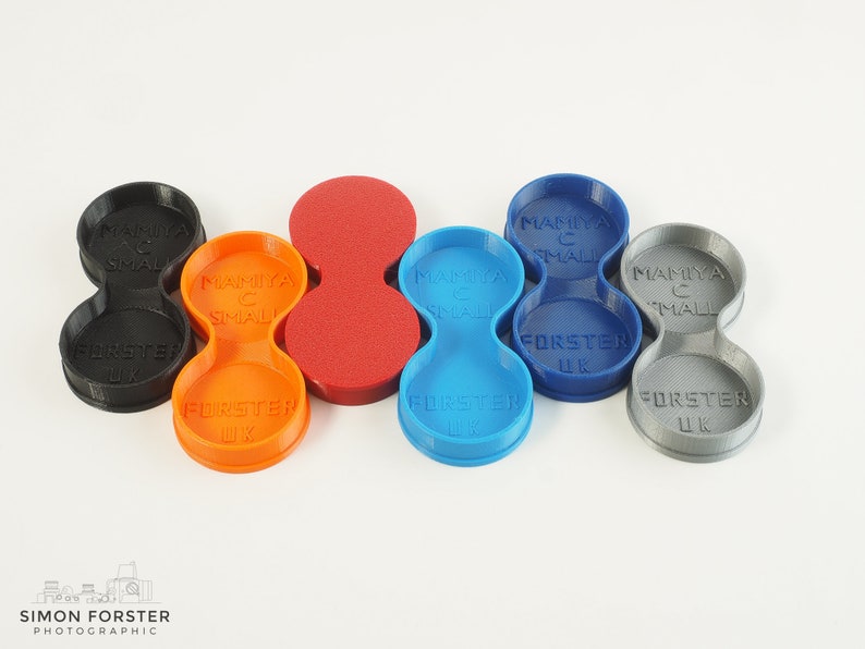 May include: Five 3D printed filter holders for small camera lenses. The holders are in black, orange, red, blue, and grey. Each holder has the text "Mamiya C Small" and "Forster UK" printed on it.