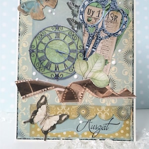 Puede incluir: Una página de álbum de recortes con un reloj azul y verde, un par de tijeras plateadas, una mariposa y una tira de película. La página está decorada con un patrón floral y la palabra "Auszeit" está escrita en cursiva.